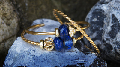 Trollbeads Gold plated bangles with blue gemstones and gold beads on a rock